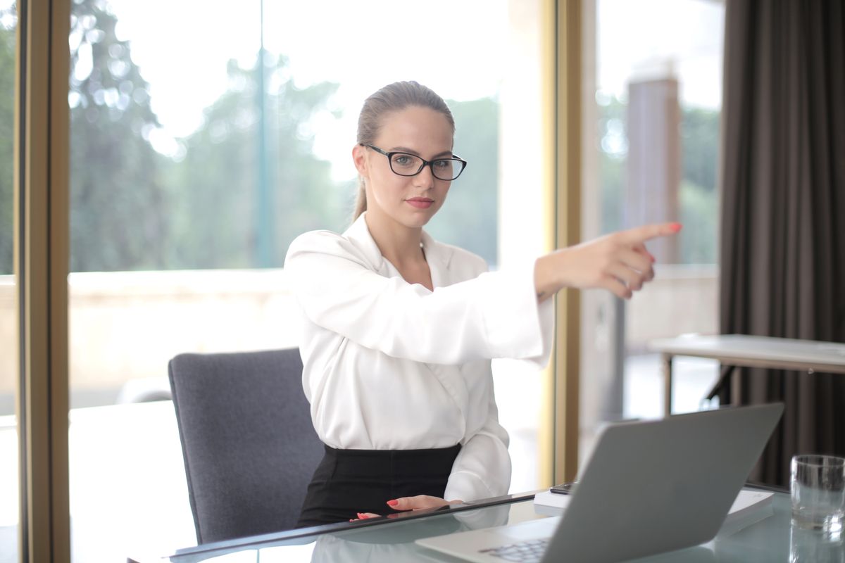 Femme d'affaires concentrée en tenue formelle et lunettes pointant du doigt devant ordinateur portable