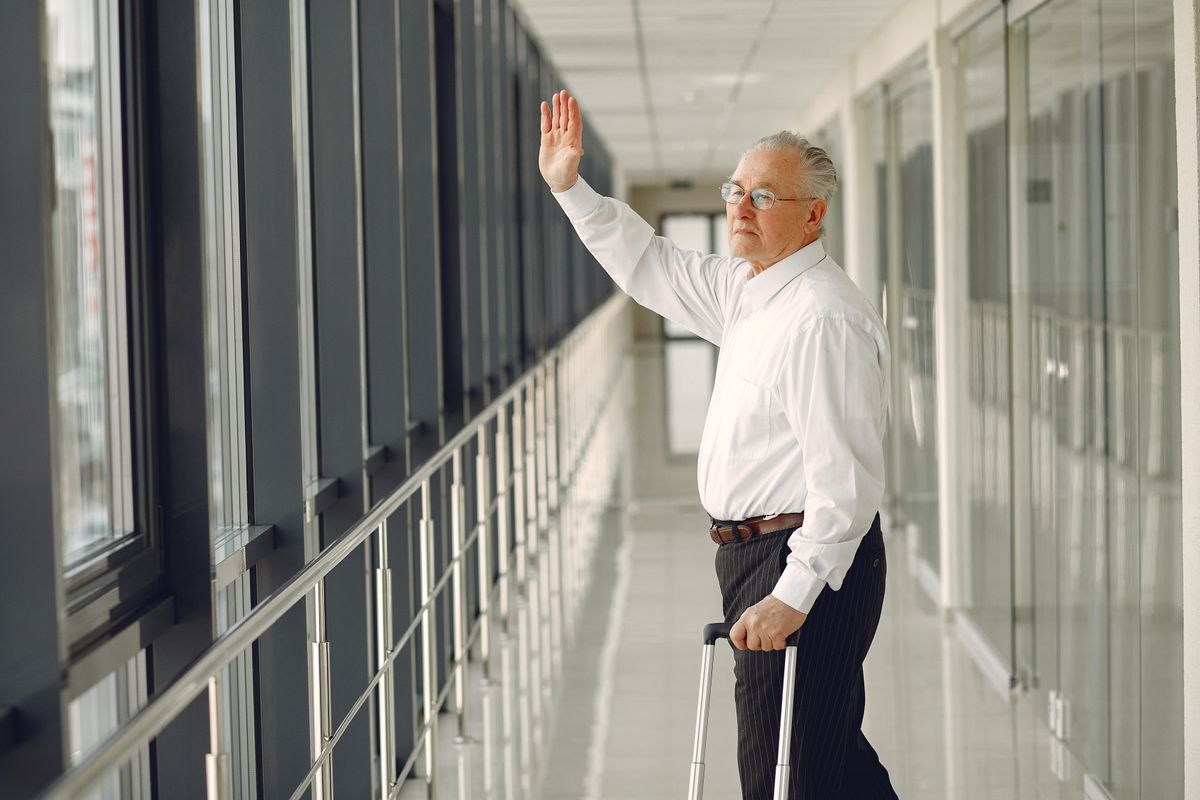 Homme en costume avec valise marchant dans un couloir d'aéroport, saluant.