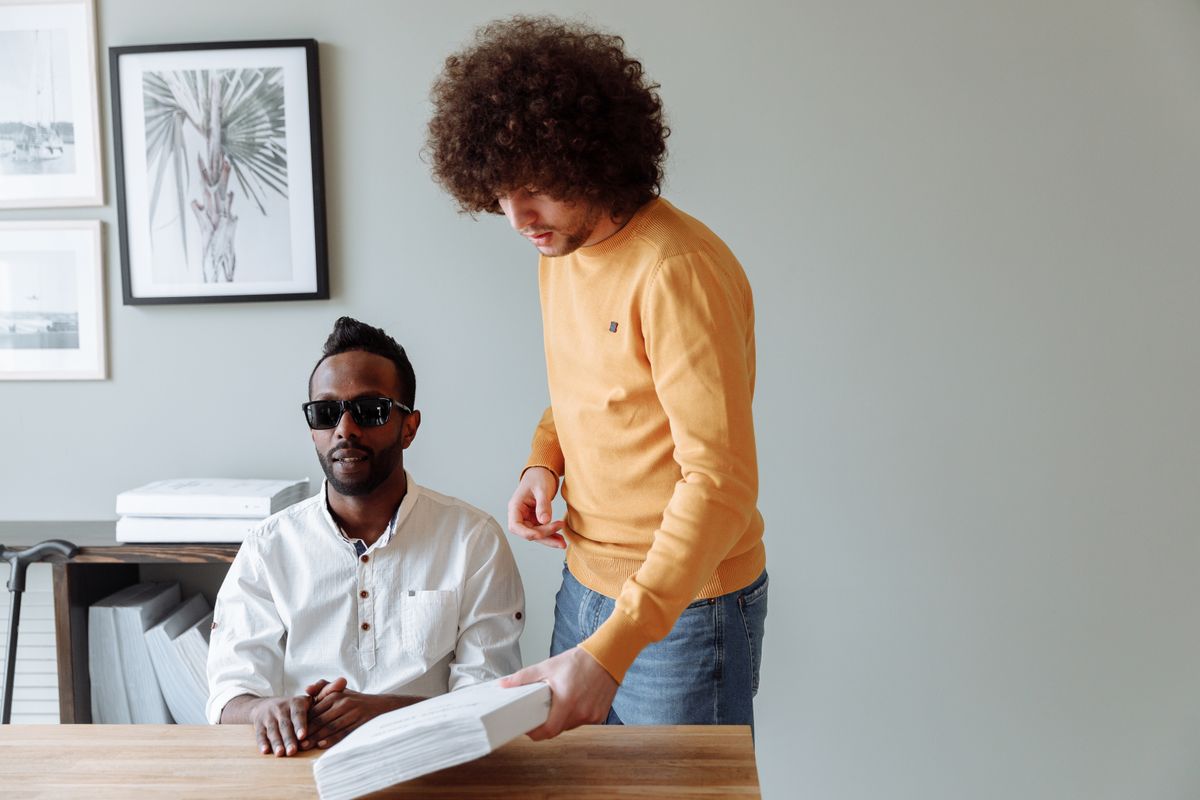 Deux hommes travaillent ensemble à un bureau, l'un portant des lunettes de soleil.
