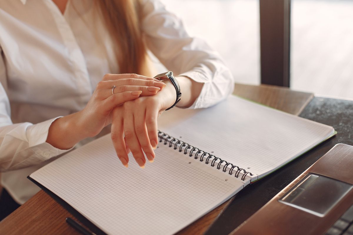 Femme en vêtements formels assise à une table regardant l'heure sur sa montre.