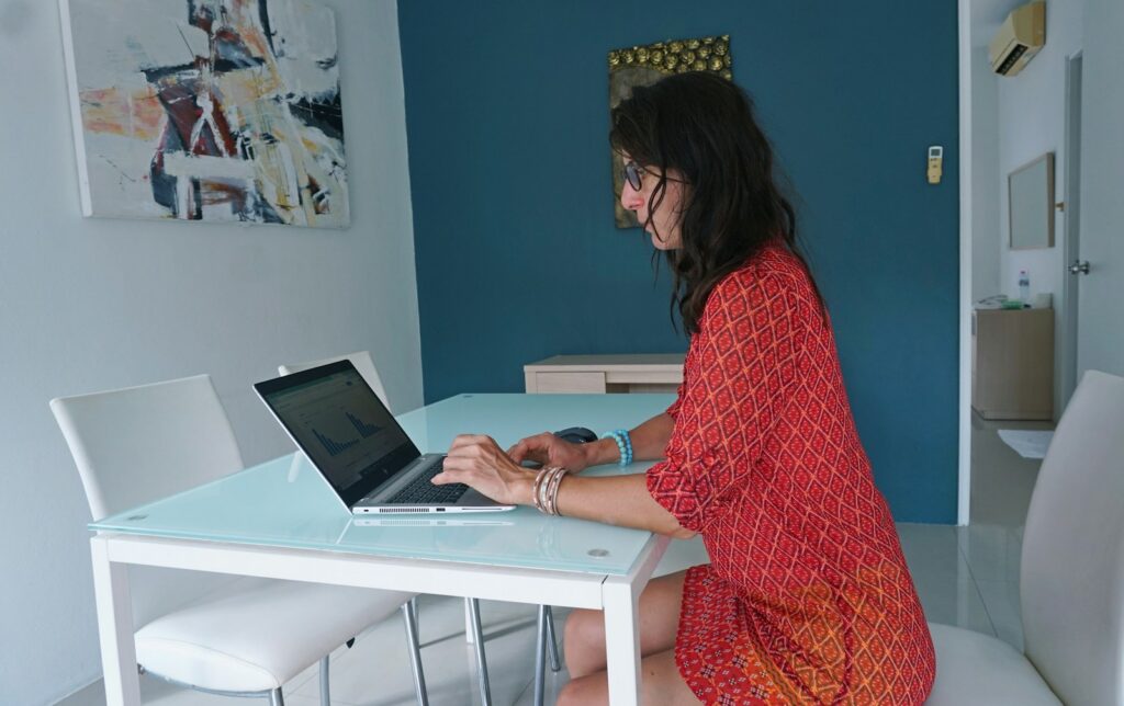 Femme en robe rouge travaillant sur un ordinateur portable à son bureau minimaliste.