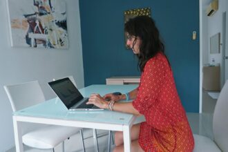 Femme en robe rouge travaillant sur un ordinateur portable à son bureau minimaliste.