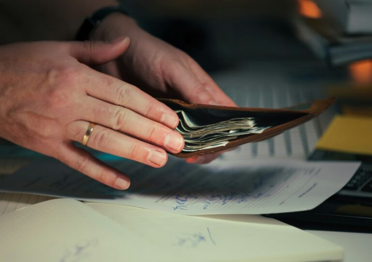 Mains tenant de l'argent dans un portefeuille au-dessus de papiers