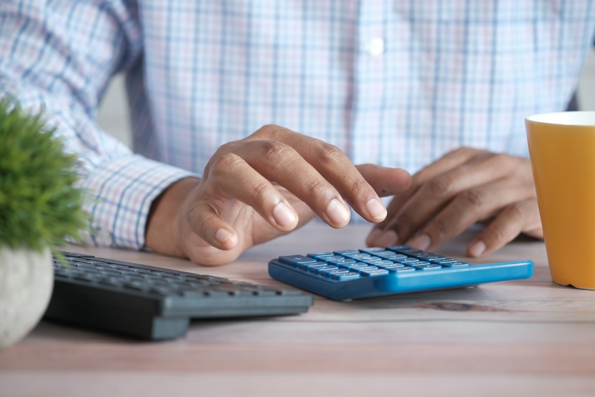 Gros plan sur une main utilisant une calculatrice près d'une tasse de café.