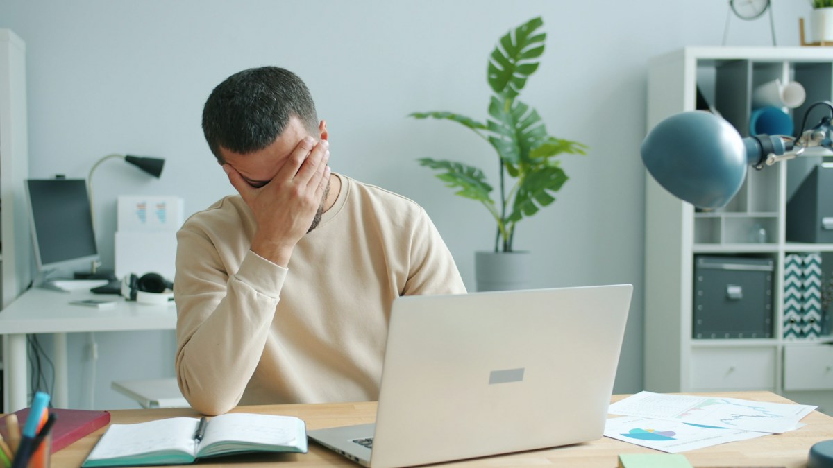 Personne épuisée au bureau touchant son visage, travaillant sur ordinateur, souffrant de mal de tête.