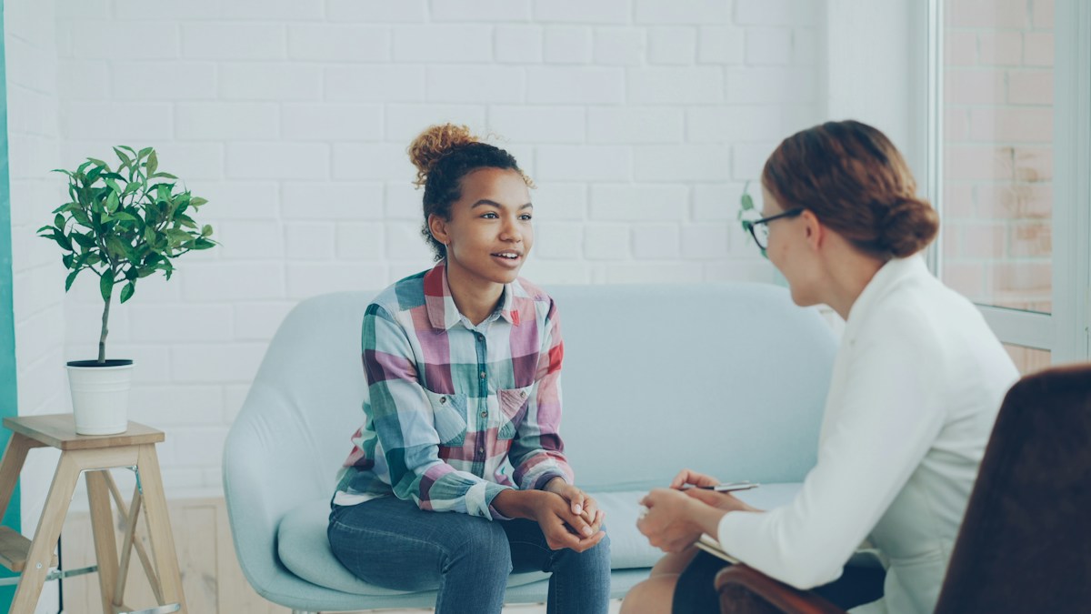 Deux femmes conversant dans un bureau moderne, l'une prenant des notes