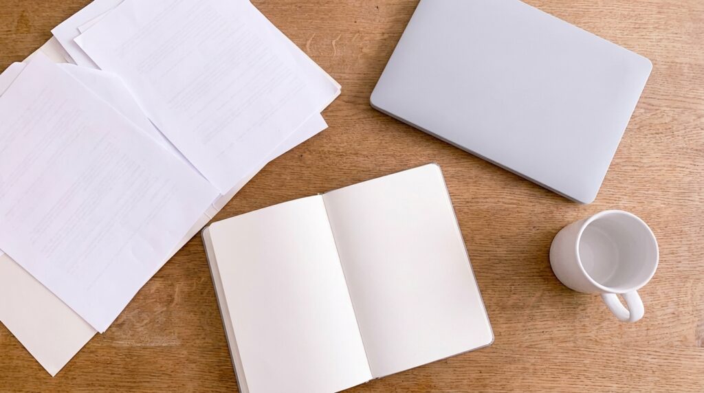 Bureau avec documents retournés, bloc-notes vierge, ordinateur portable gris et tasse de café
