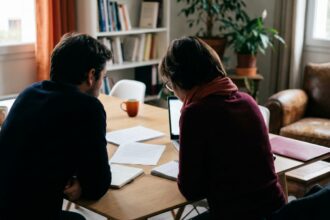 Deux personnes penchées vers une table en bois clair, écoutant attentivement.