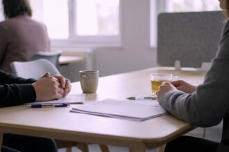 Bureau de réunion avec documents éparpillés, stylos, tasses et deux paires de mains