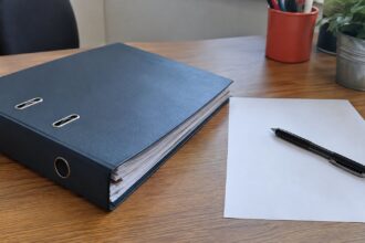 Dossier fermé et stylo noir sur bureau en bois avec feuille blanche.