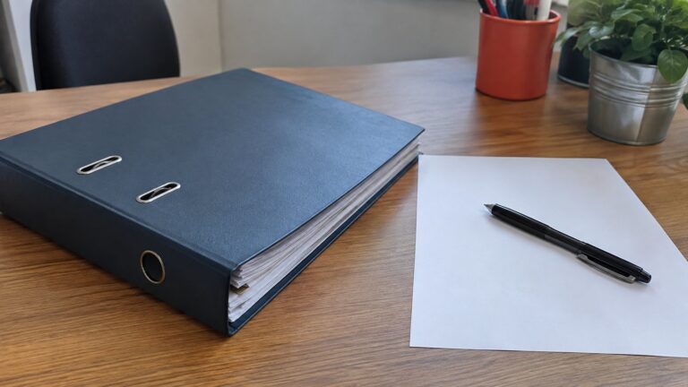 Dossier fermé et stylo noir sur bureau en bois avec feuille blanche.
