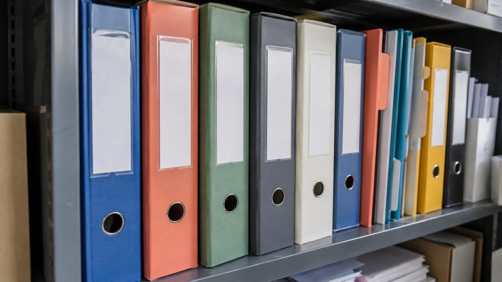 Dossiers de classement de couleurs variées rangés verticalement sur une étagère métallique.