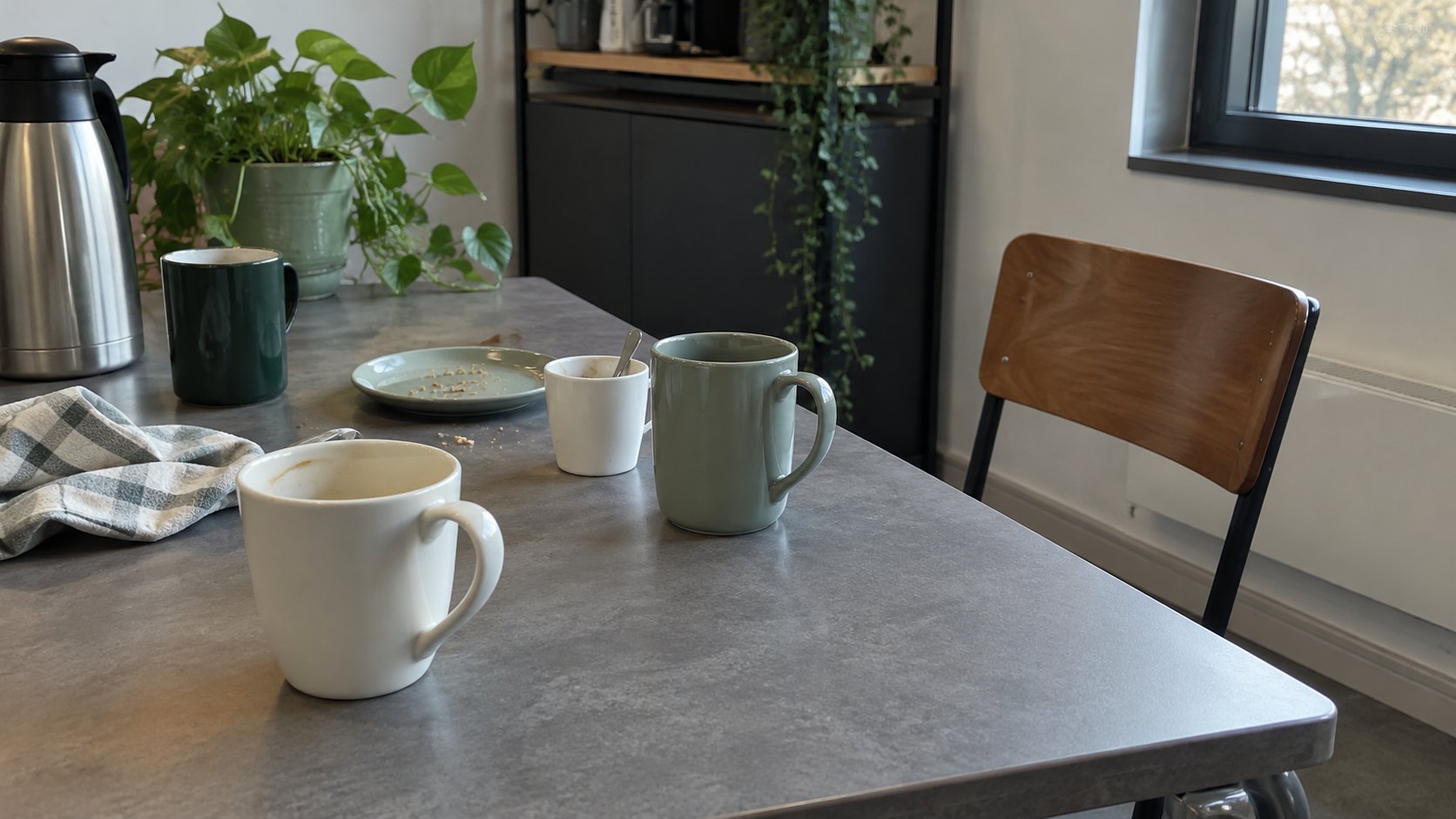Détail d'une table de pause avec tasses abandonnées, chaise isolée et surface grise.
