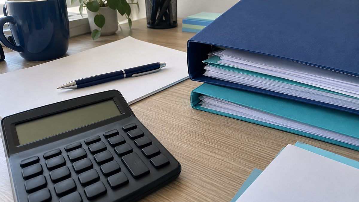 Gros plan sur un poste de travail administratif avec calculatrice, dossiers et documents.