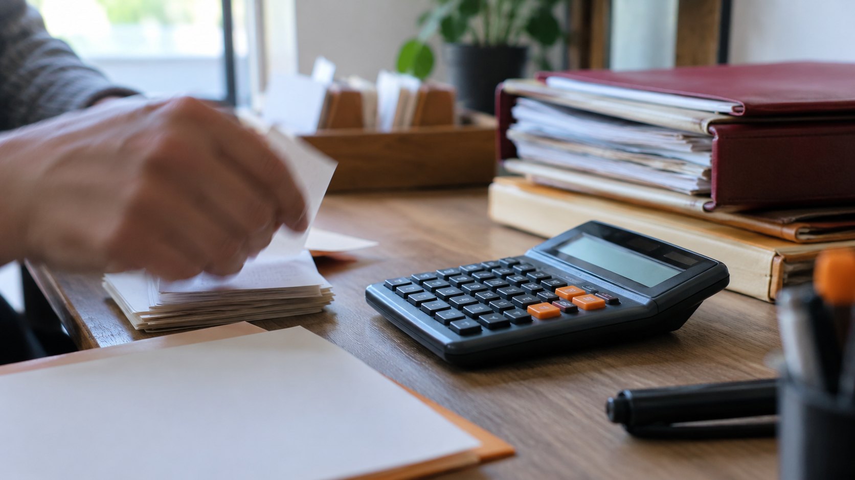 Gros plan sur calculatrice, dossiers et fiches empilées avec main floue