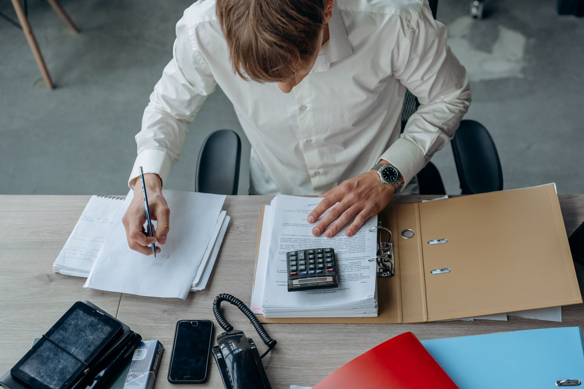 Une personne vérifie des documents à son bureau avec une calculatrice, vue du dessus.