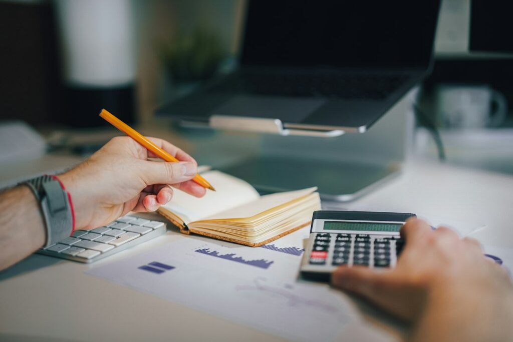 Une personne utilise une calculatrice à son bureau, à côté d’un ordinateur et d’un carnet.
